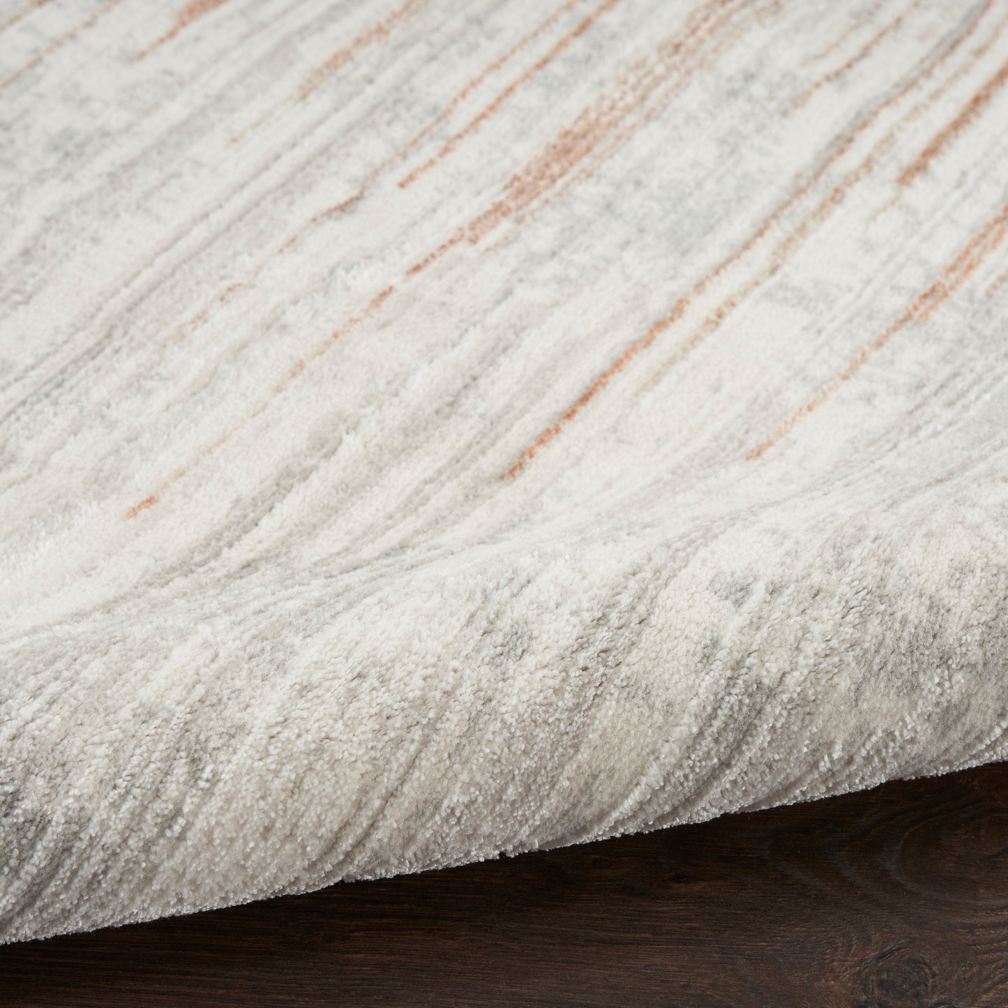 Close-up of a light gray and cream marbled rug with subtle orange streaks on dark wood floor.