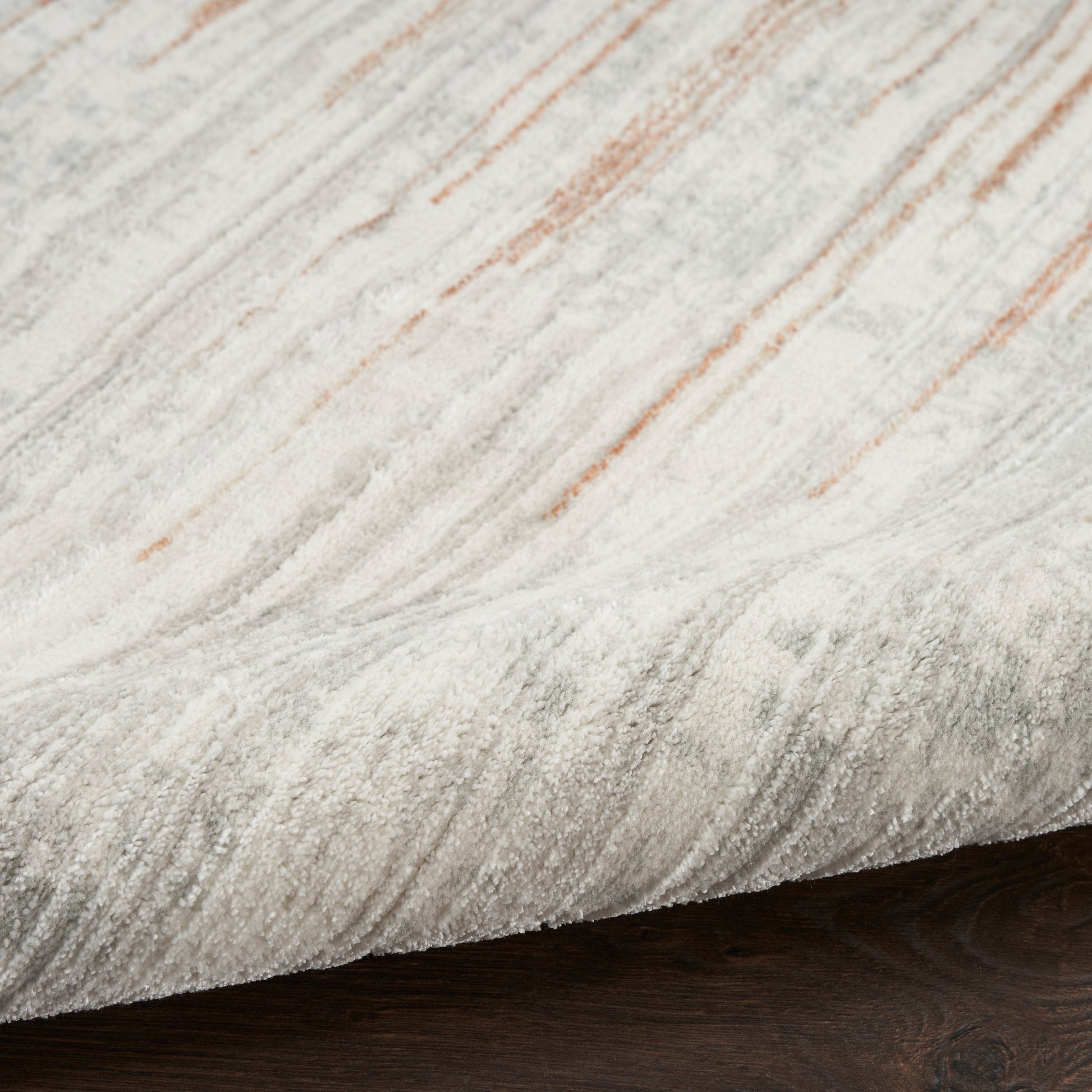 Close-up of a light gray and cream marbled rug with subtle orange streaks on dark wood floor.