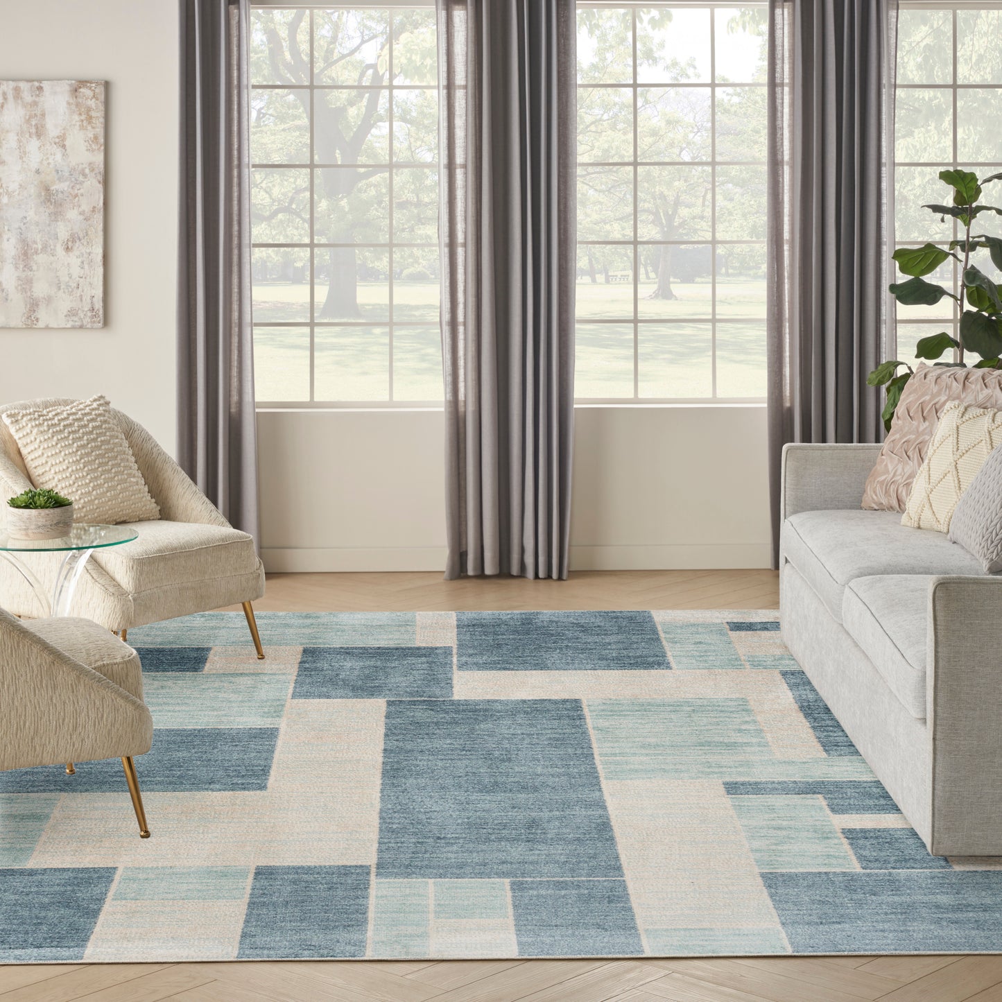Geometric area rug in blue, gray and beige tones in a bright living room with a gray sofa and beige chairs.