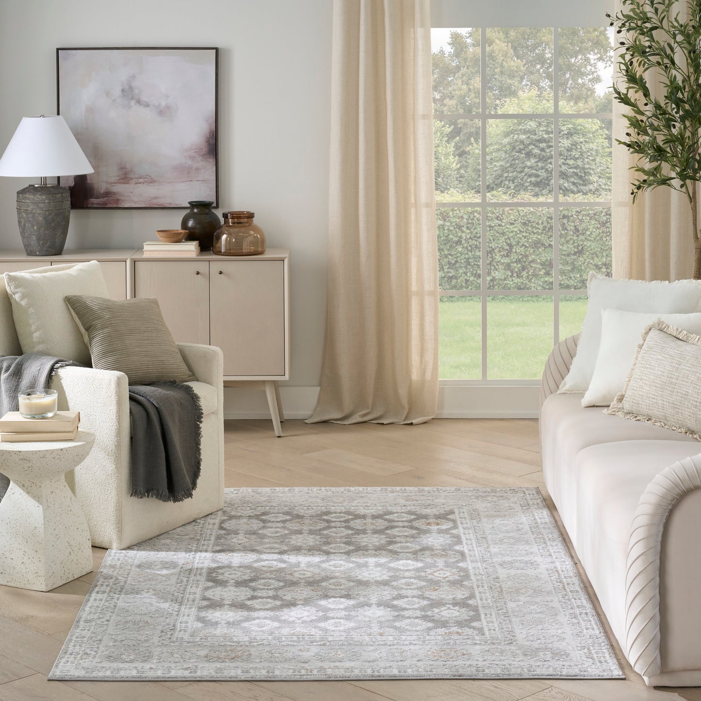 Soft gray geometric area rug in a neutral living room with cream sofa, beige curtains, and light wood flooring.