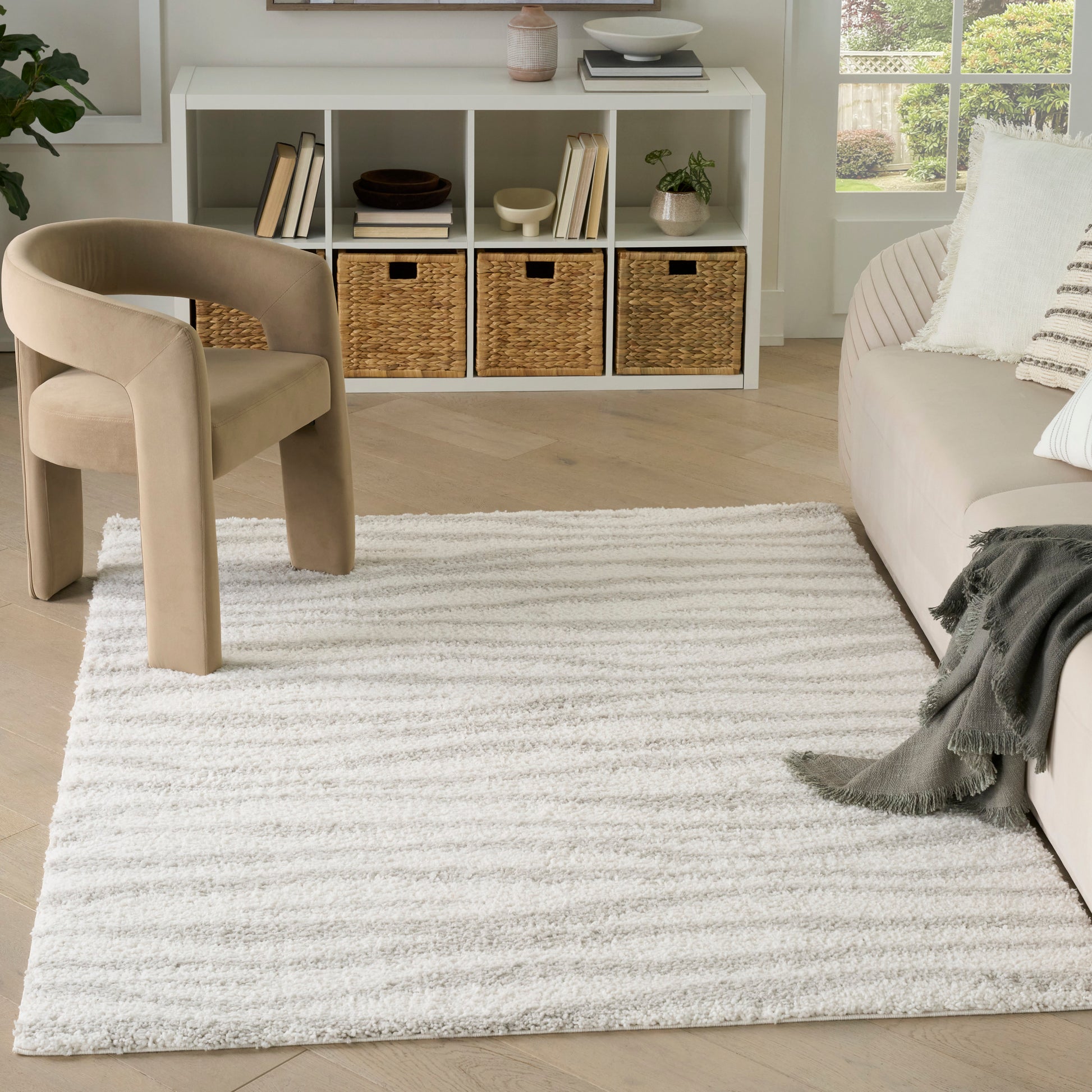 Soft textured white & light gray striped area rug on light wood floor, with beige curved chair & white cubby storage.