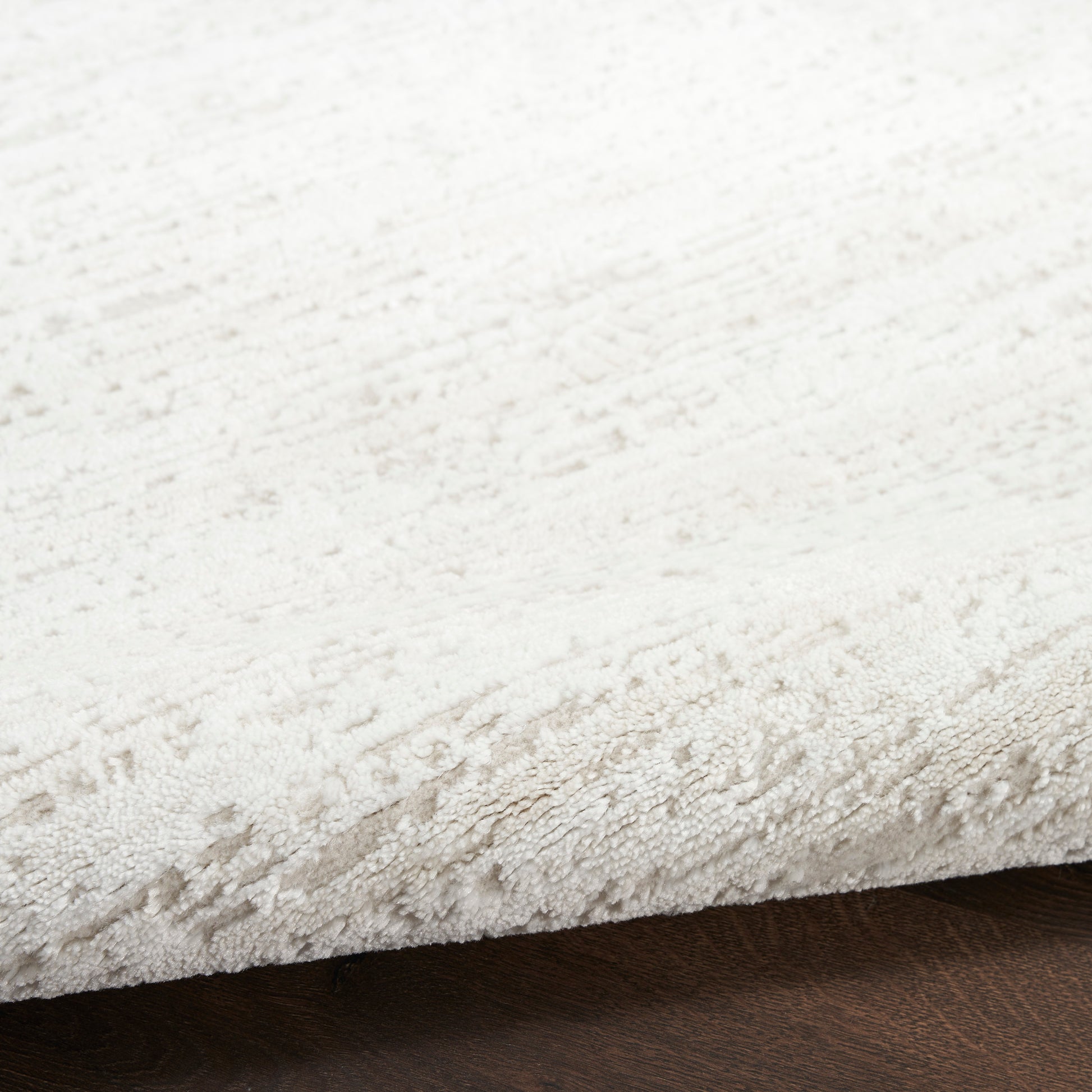Cream plush rug with subtle textured pattern and soft pile on dark wood floor.