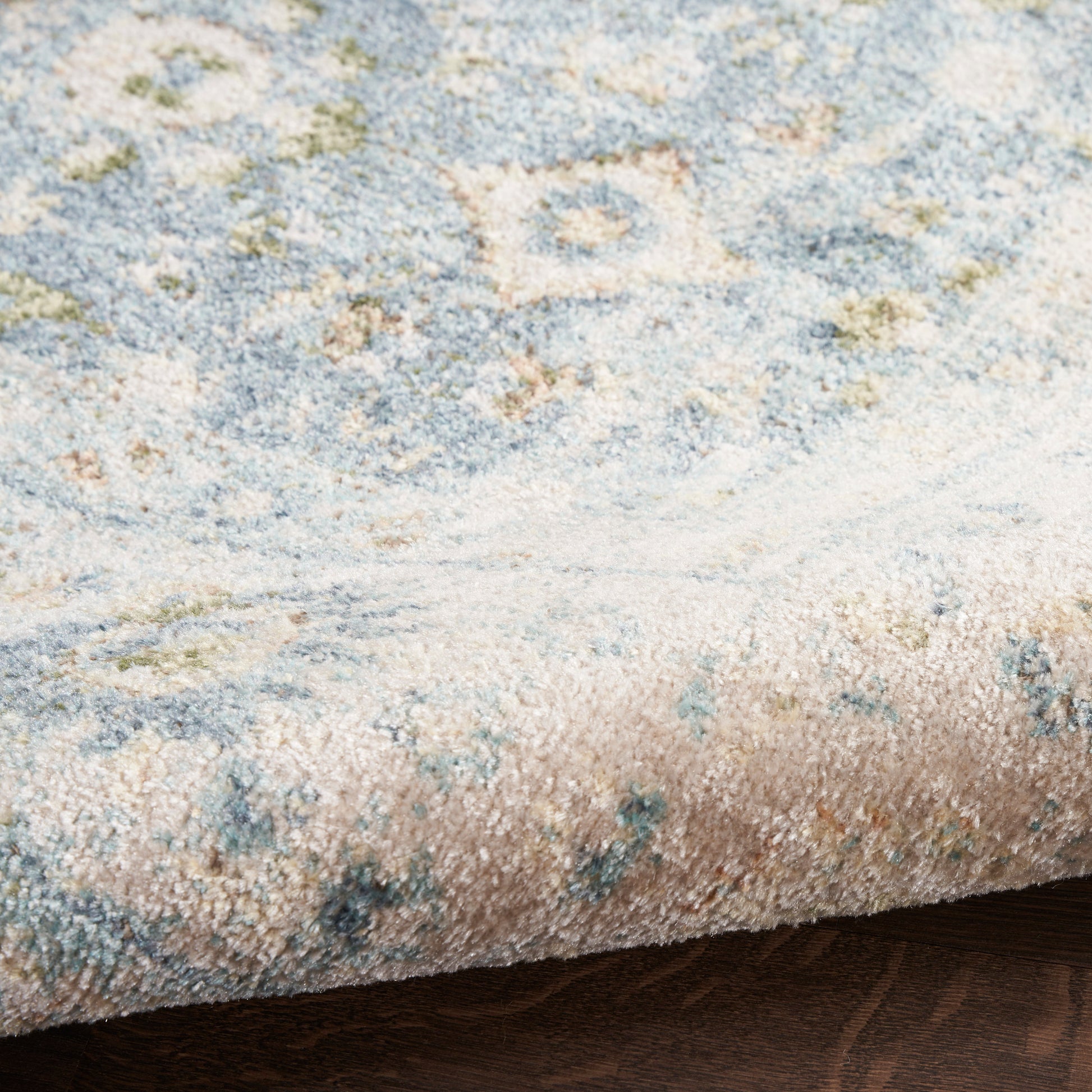 Soft blue and ivory abstract floral area rug with muted beige accents and a rolled edge on wood floor.