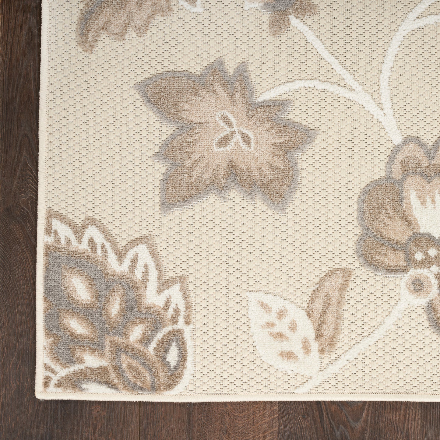 Cream woven area rug with taupe floral motif and subtle border on dark wood floor.