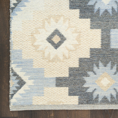 Kilim-style area rug with cream, light blue and navy geometric sunburst motifs on a dark wood floor.