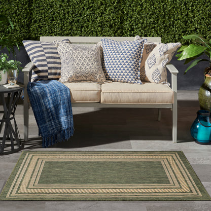 Outdoor beige rug with a green multi-border pattern (3' x 5') on a patio with plants; nearby seating with cushions and a blue throw.