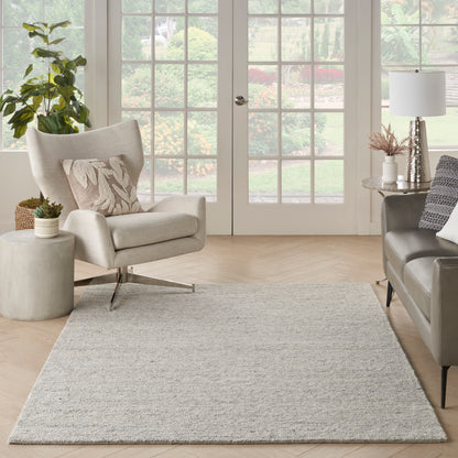 Light beige fabric armchair, gray sofa, textured neutral rug, potted plant, & white French doors in a bright living room.