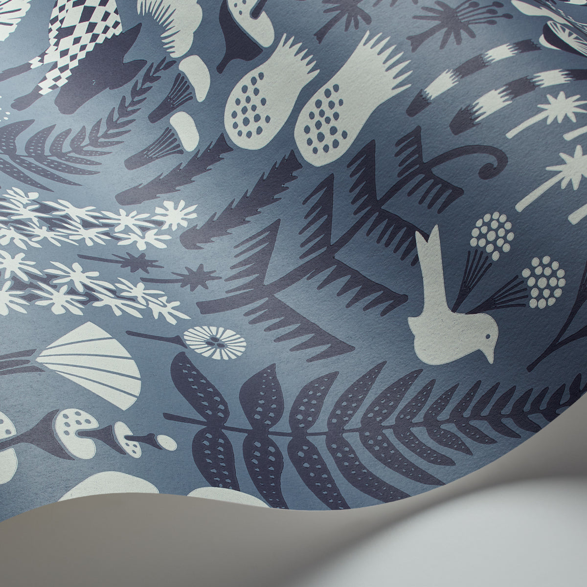 Close-up of blue fabric with white and pale-blue botanical print featuring ferns, leaves, birds and abstract shapes.