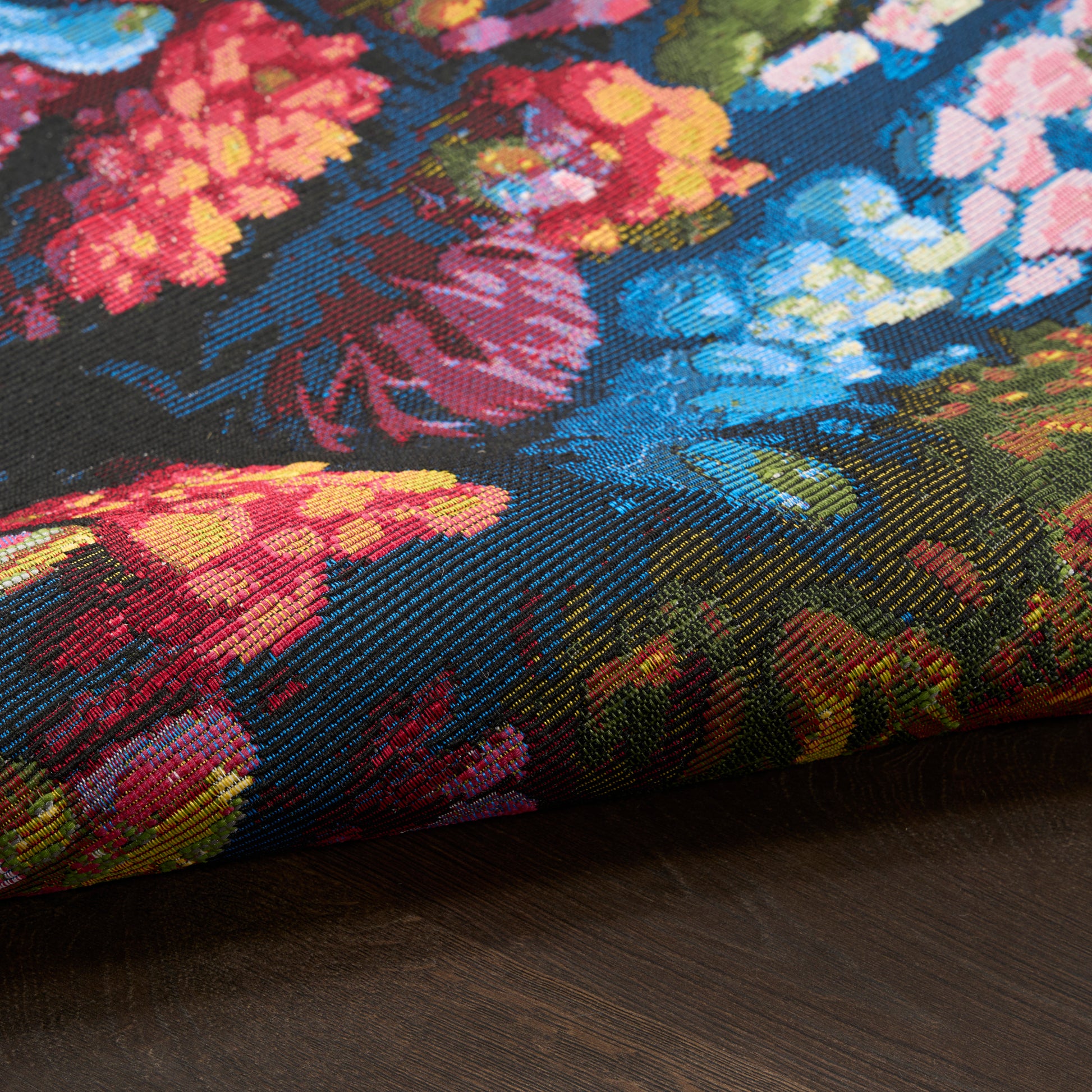 Close-up of colorful floral rug with blue background and bright pink, red and yellow flowers on a dark wooden surface.
