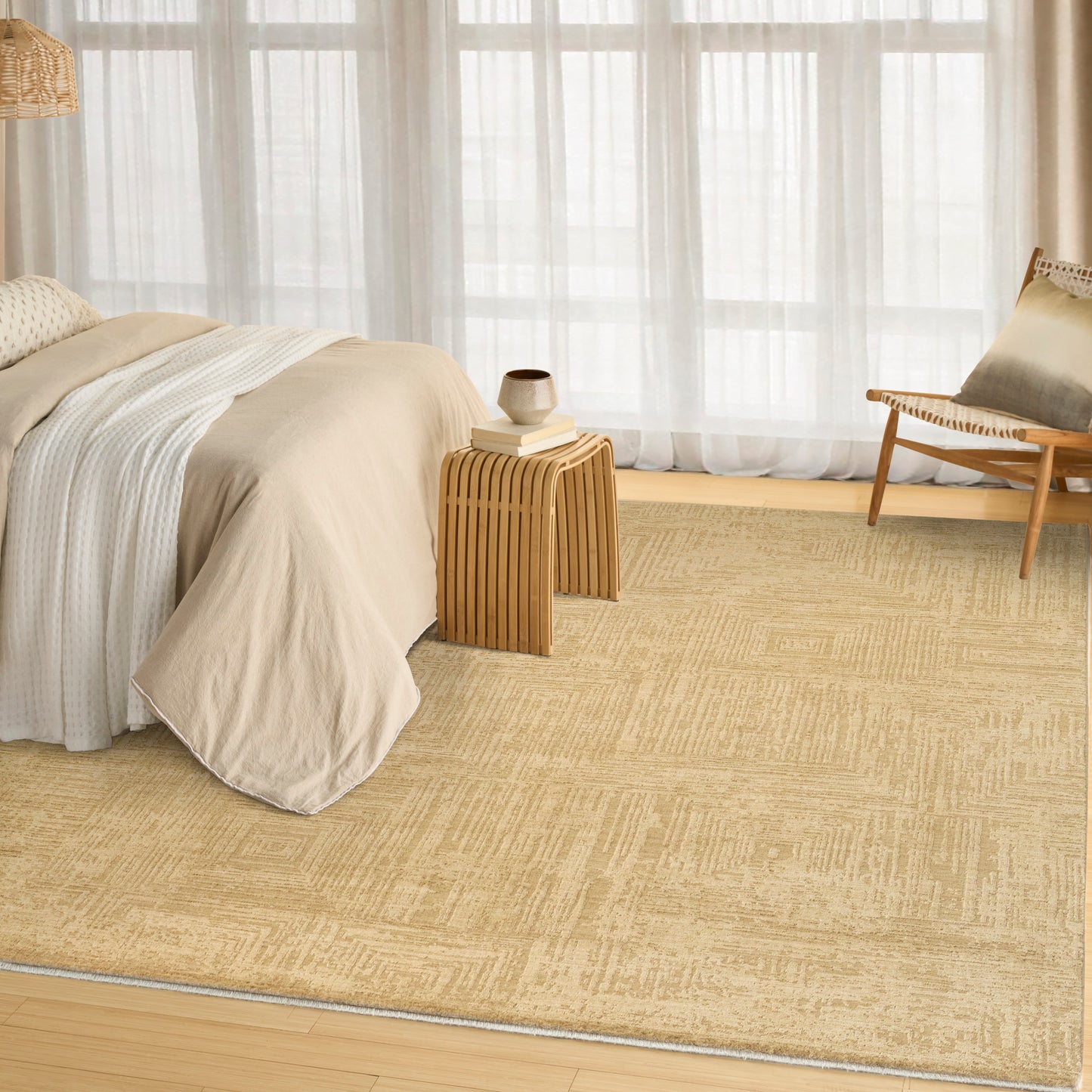Neutral bedroom with beige bedding, woven jute rug, light wood side tables, and a wooden lounge chair by sheer curtains.