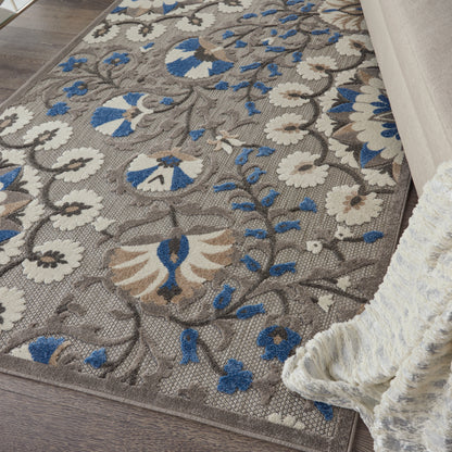 Taupe floral area rug with cream and blue blossoms and scrolling vines on a wood floor.