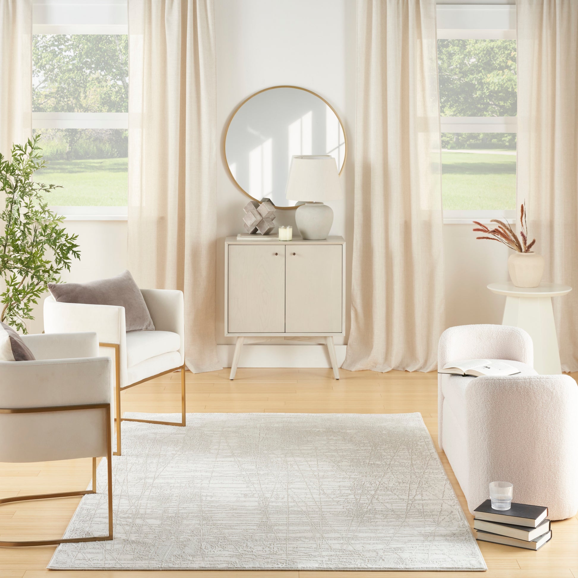 Bright neutral living room with cream seating, light wood cabinet, round mirror, beige curtains, rug, and potted greenery.
