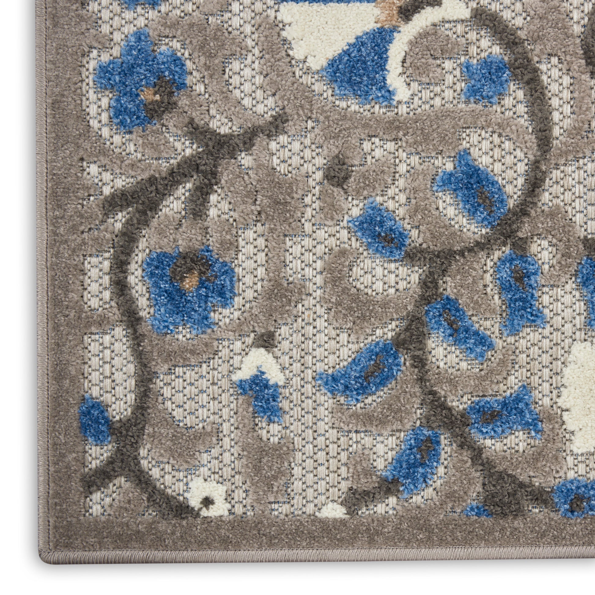 Close-up of a gray-beige floral area rug with blue flowers and brown vines, woven texture.