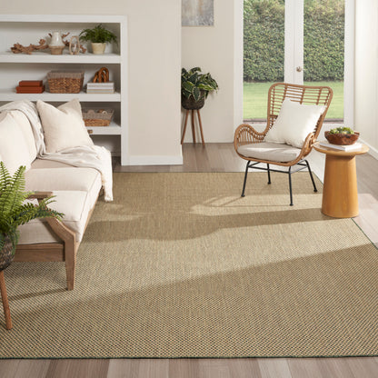 Neutral living room with a beige woven rug, cream sofa, rattan chair, wooden side table, plants, and glass doors.
