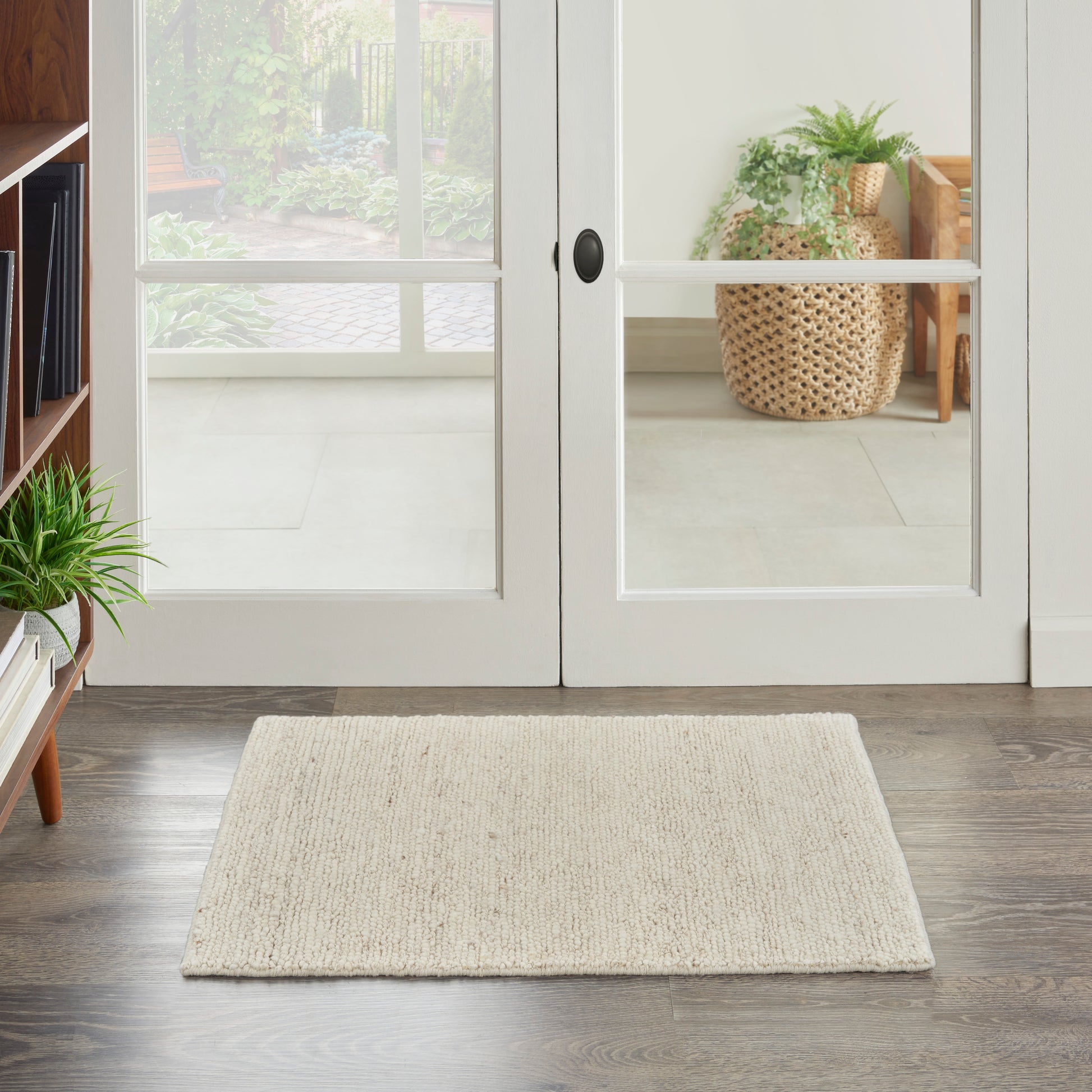 Cream woven rectangular entryway rug in front of white-framed glass doors on dark wood floor.