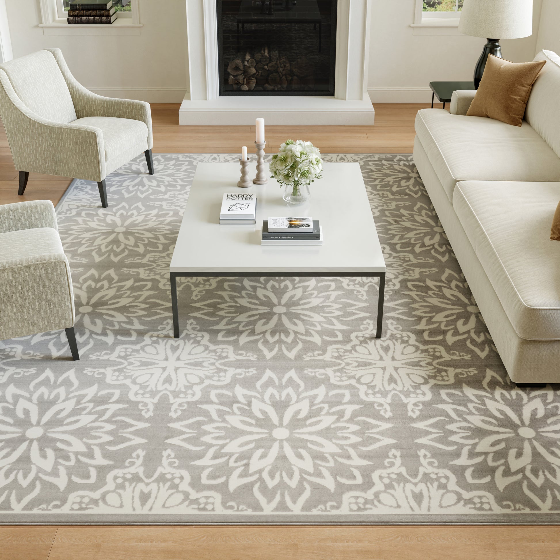 Contemporary living room with a gray and white floral rug, white square coffee table, cream sofa and chairs, fireplace.