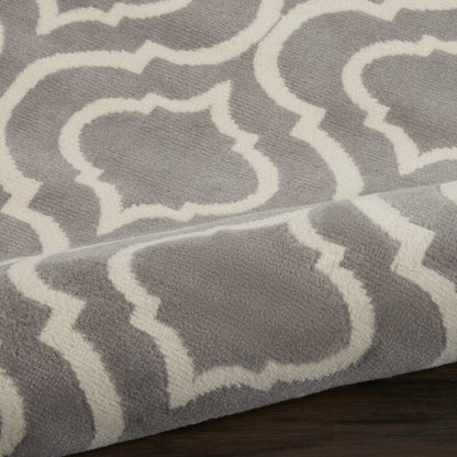 Gray plush rug with white trellis/quatrefoil pattern; soft pile, folded edge on dark wood floor.