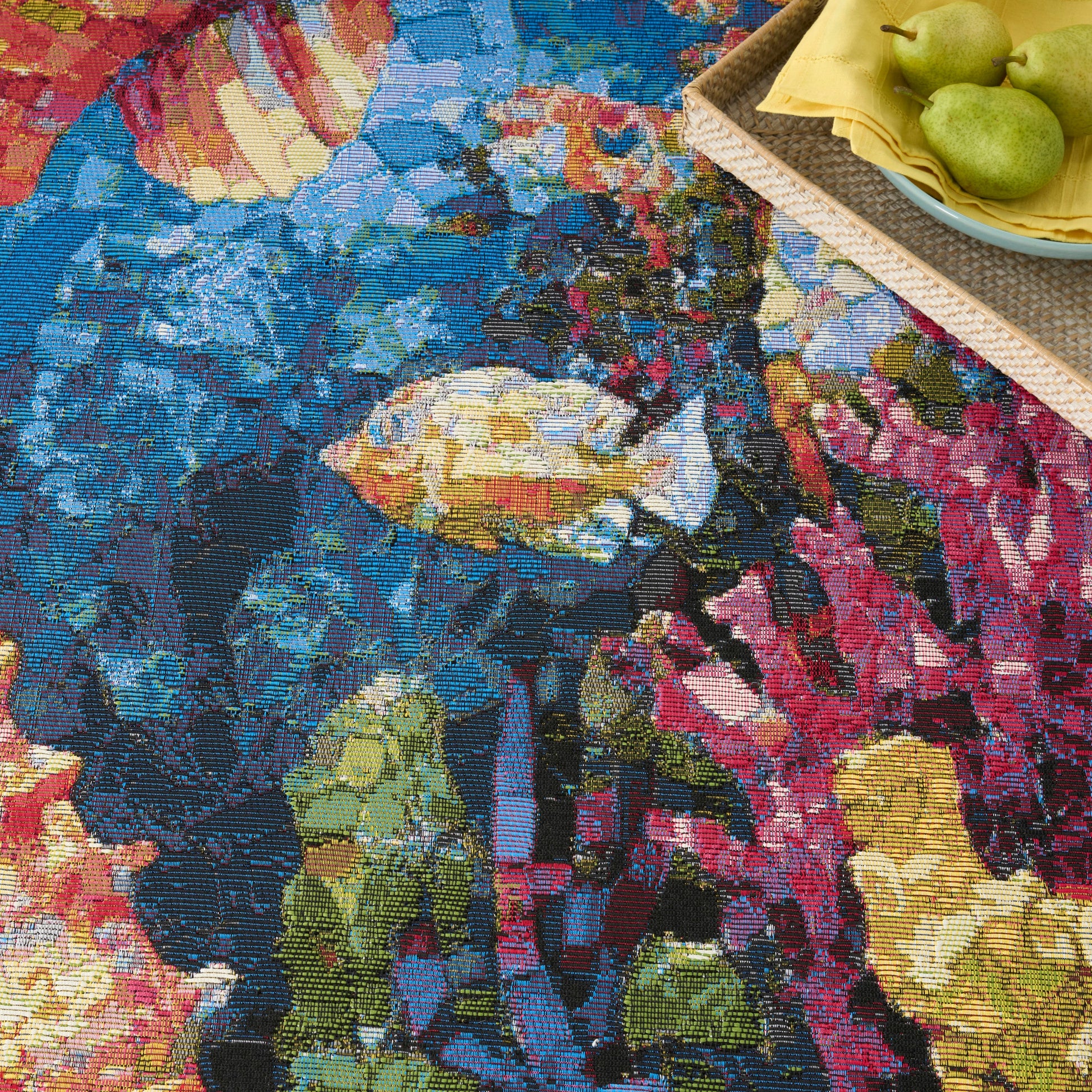 Colorful woven floral tapestry rug in blues, pinks and yellows; corner basket with pears on a yellow napkin.