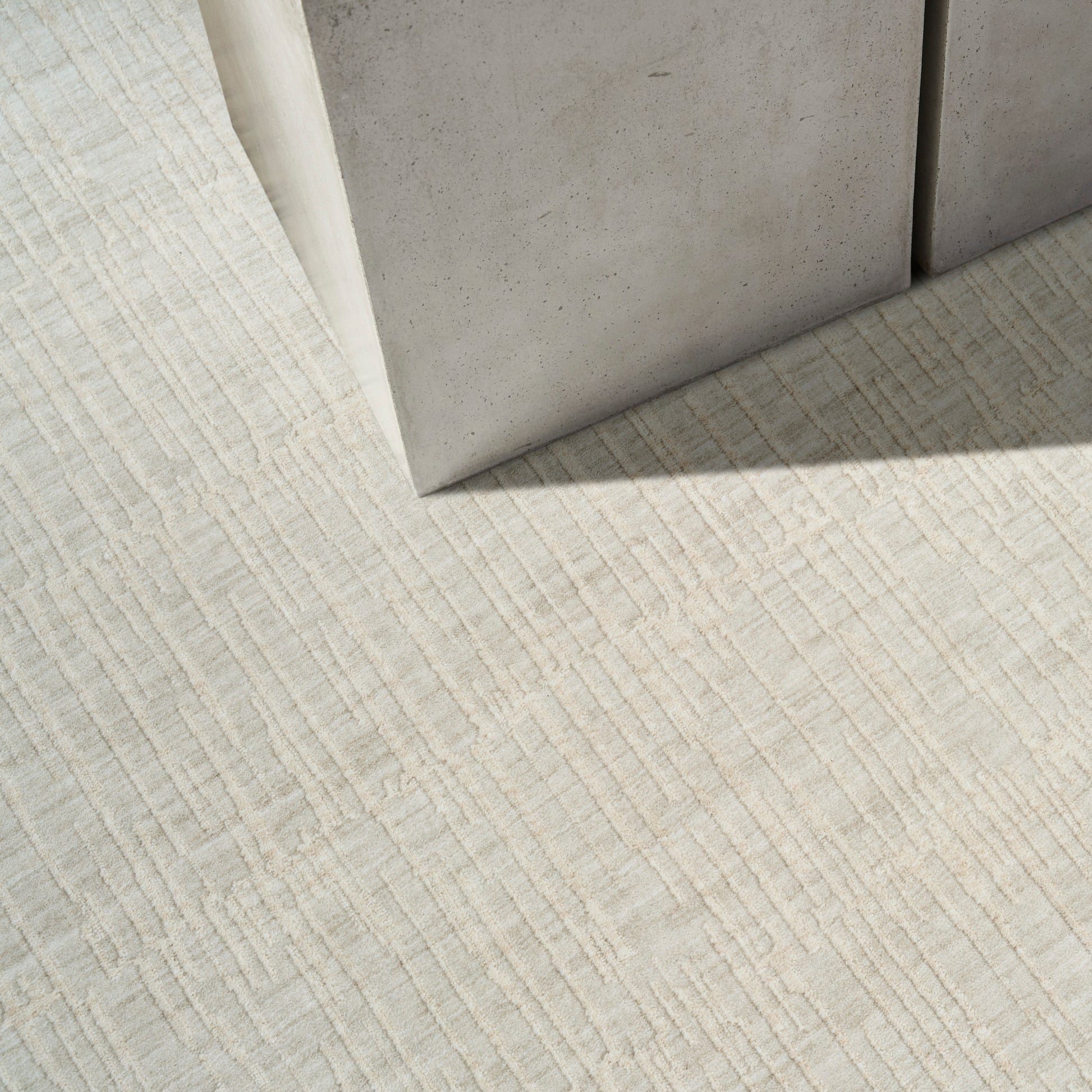 Ivory textured rug with raised linear grid pattern beside gray concrete blocks.