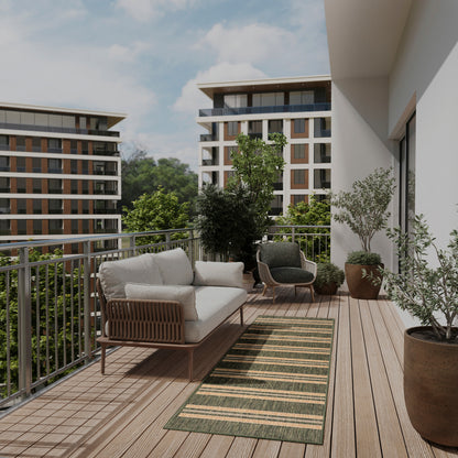 Wooden balcony deck with cream cushioned wicker sofa, dark wicker chair, green striped rug, potted trees, metal railing.