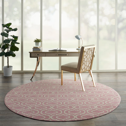 Round pink rug with white geometric pattern under a wooden desk and beige upholstered chair in a sunlit home office.