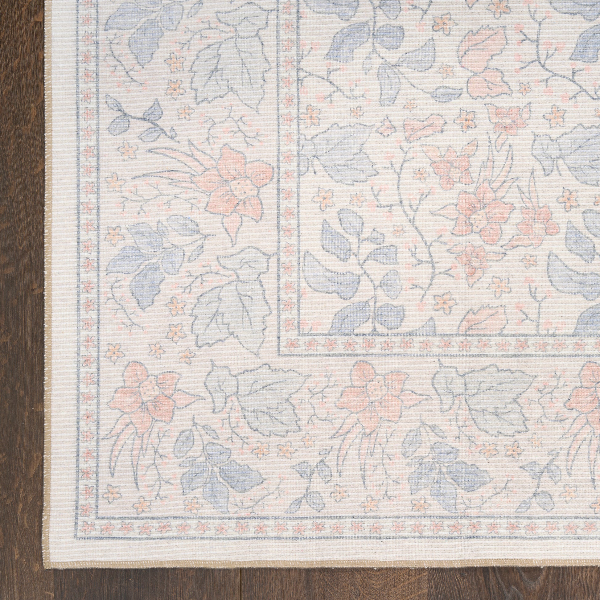 Pastel floral rug with blue and peach blossoms, framed border, on a wooden floor.