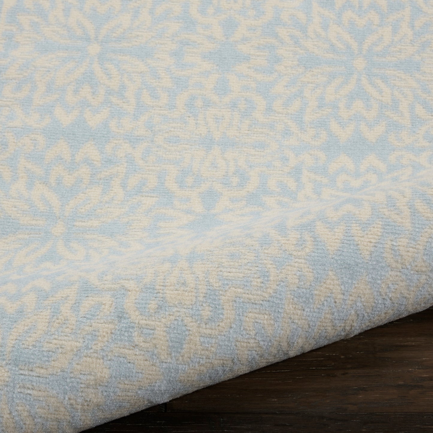 Light blue rug with cream damask jacquard pattern, folded over a dark wood surface.