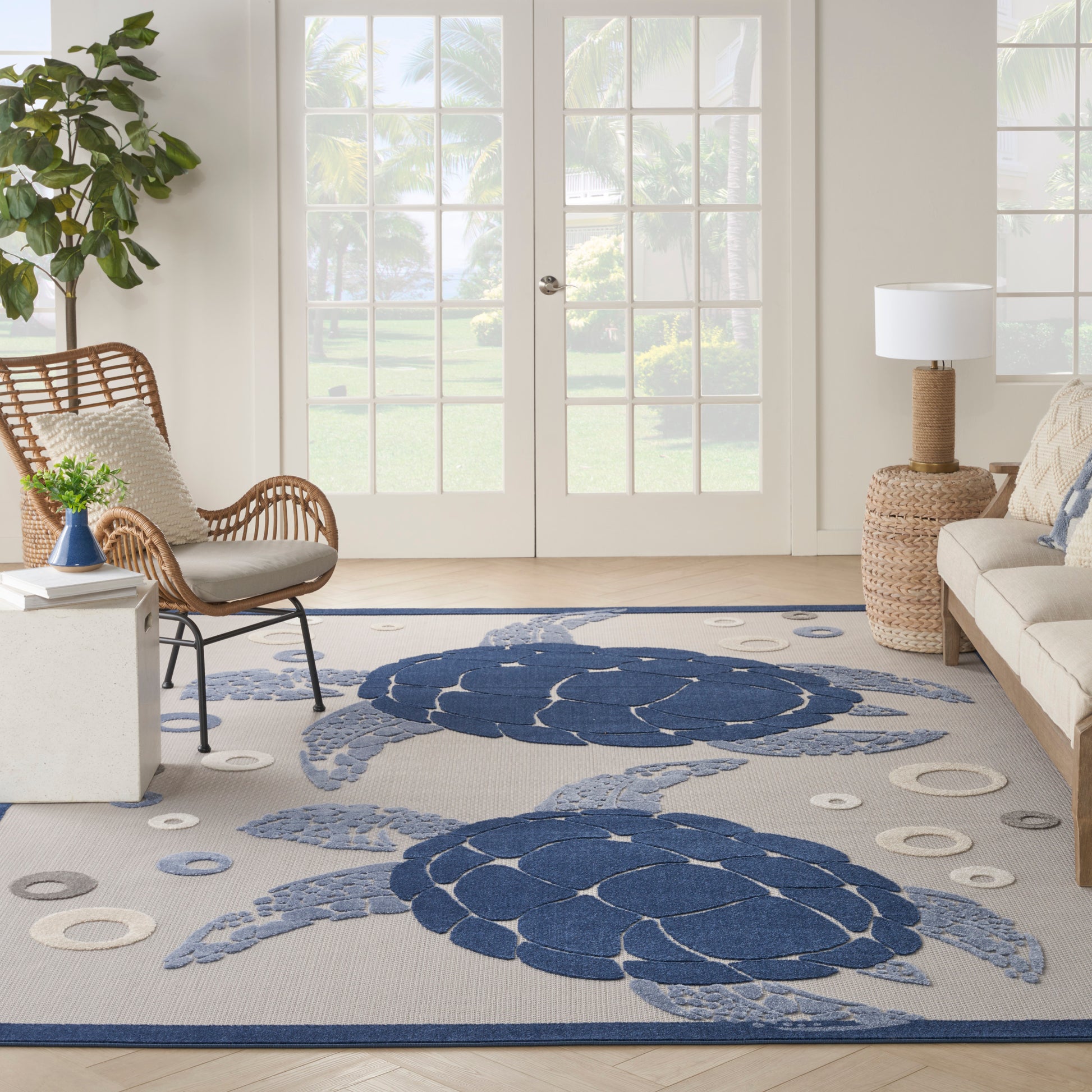 Coastal beige area rug with large navy sea turtle motifs, in a bright living room with wicker chair and glass doors.