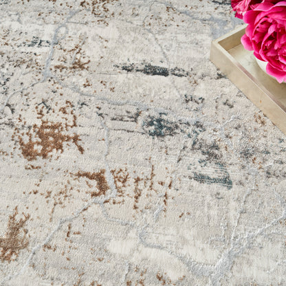 Beige woven area rug with abstract brown and blue patterns, beside a wooden tray holding bright pink peonies.