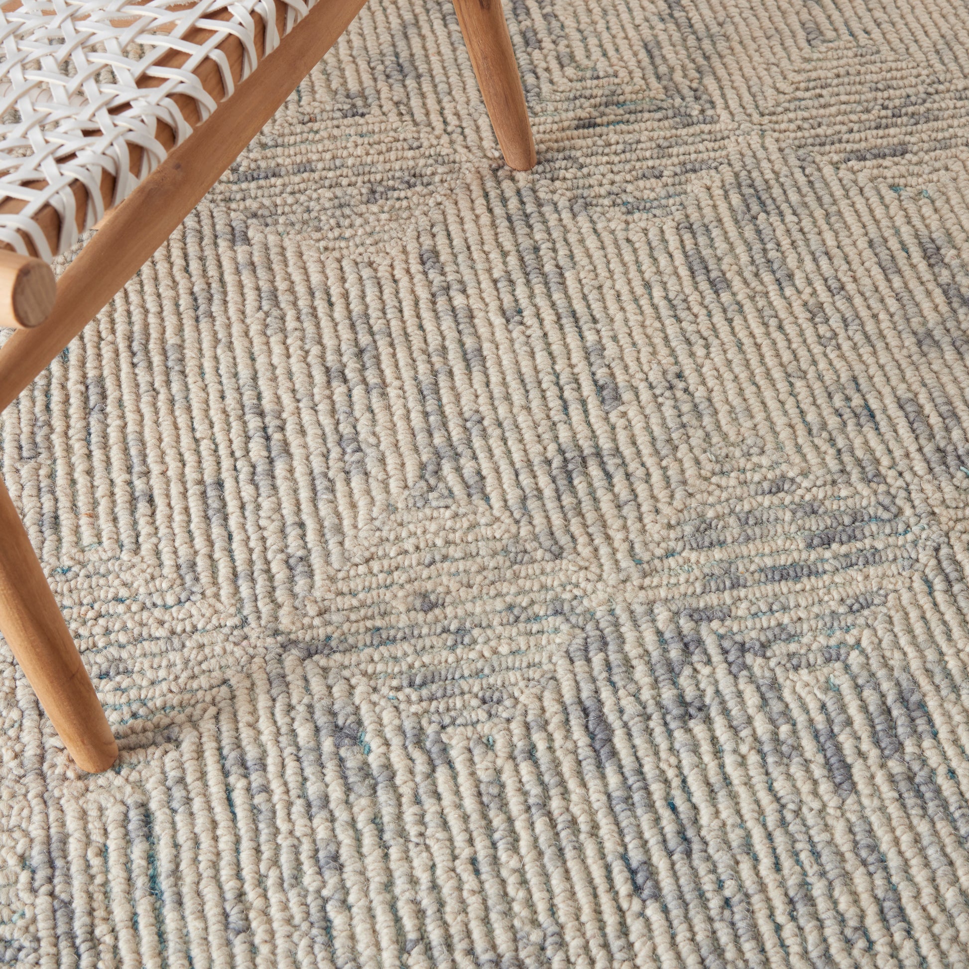Beige woven rug with subtle blue accents and linear geometric pattern; wooden chair legs visible.
