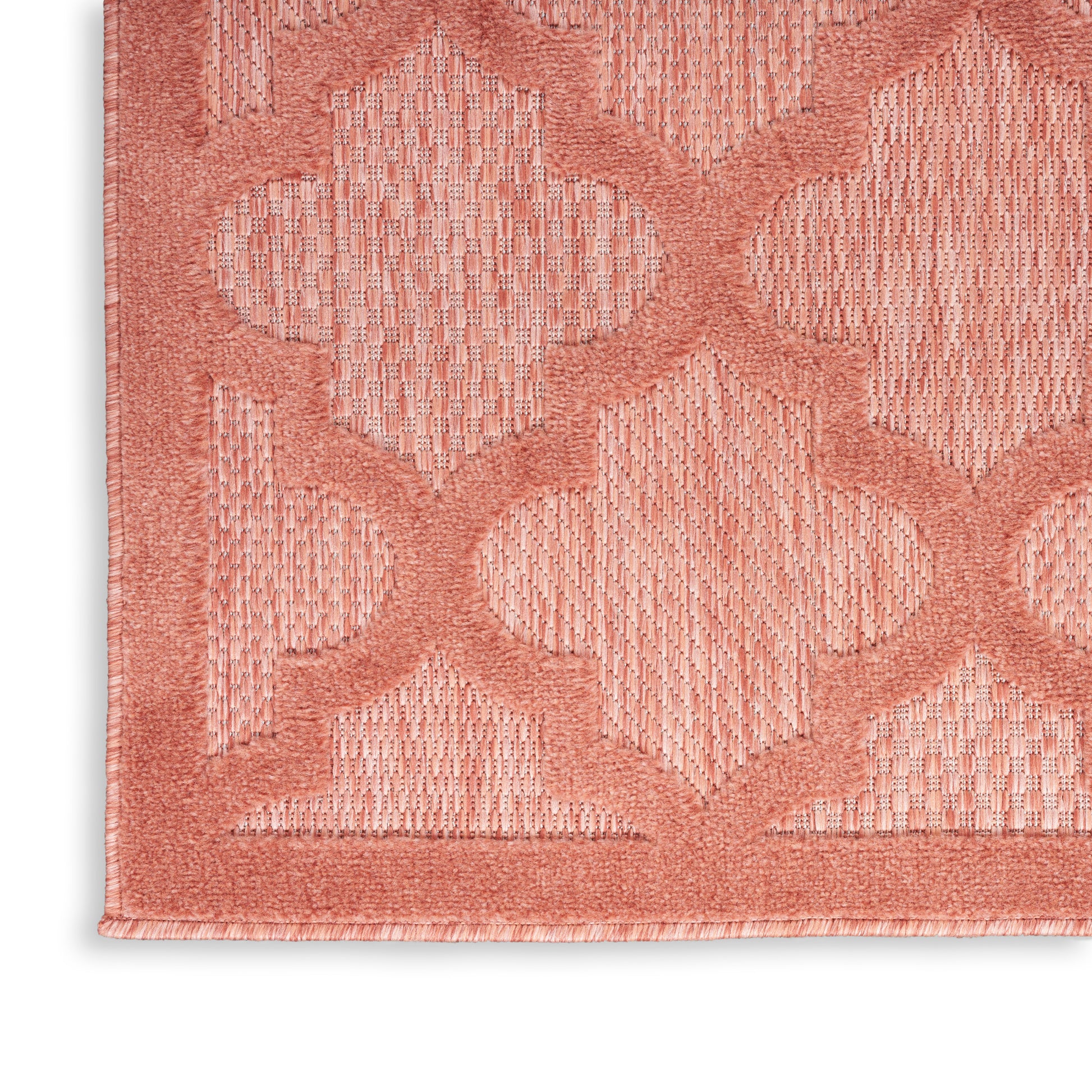 Coral-pink textured rug with interlocking trellis/clover pattern and fringe along the edge.