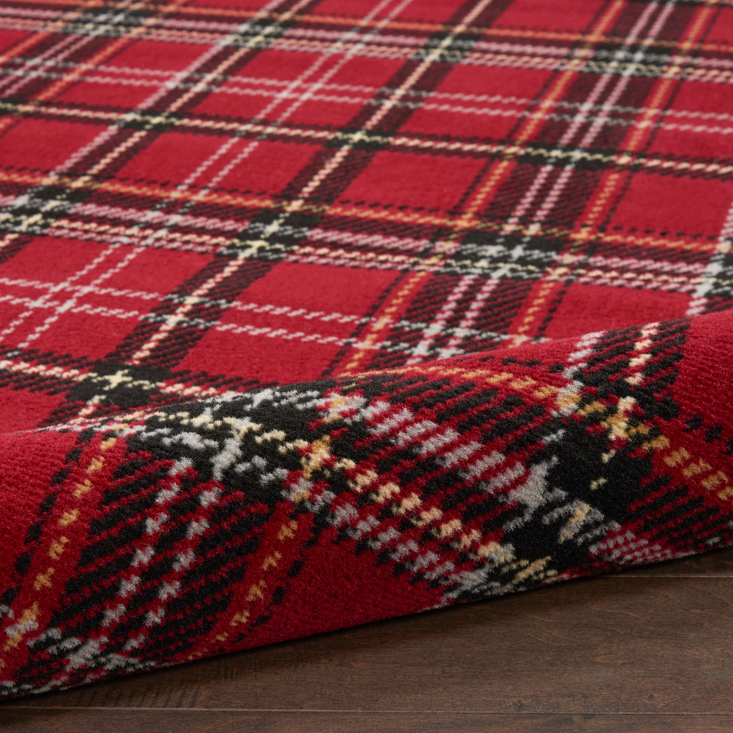 Red plaid tartan rug with black, white & yellow lines, soft pile, folded on a wooden floor.