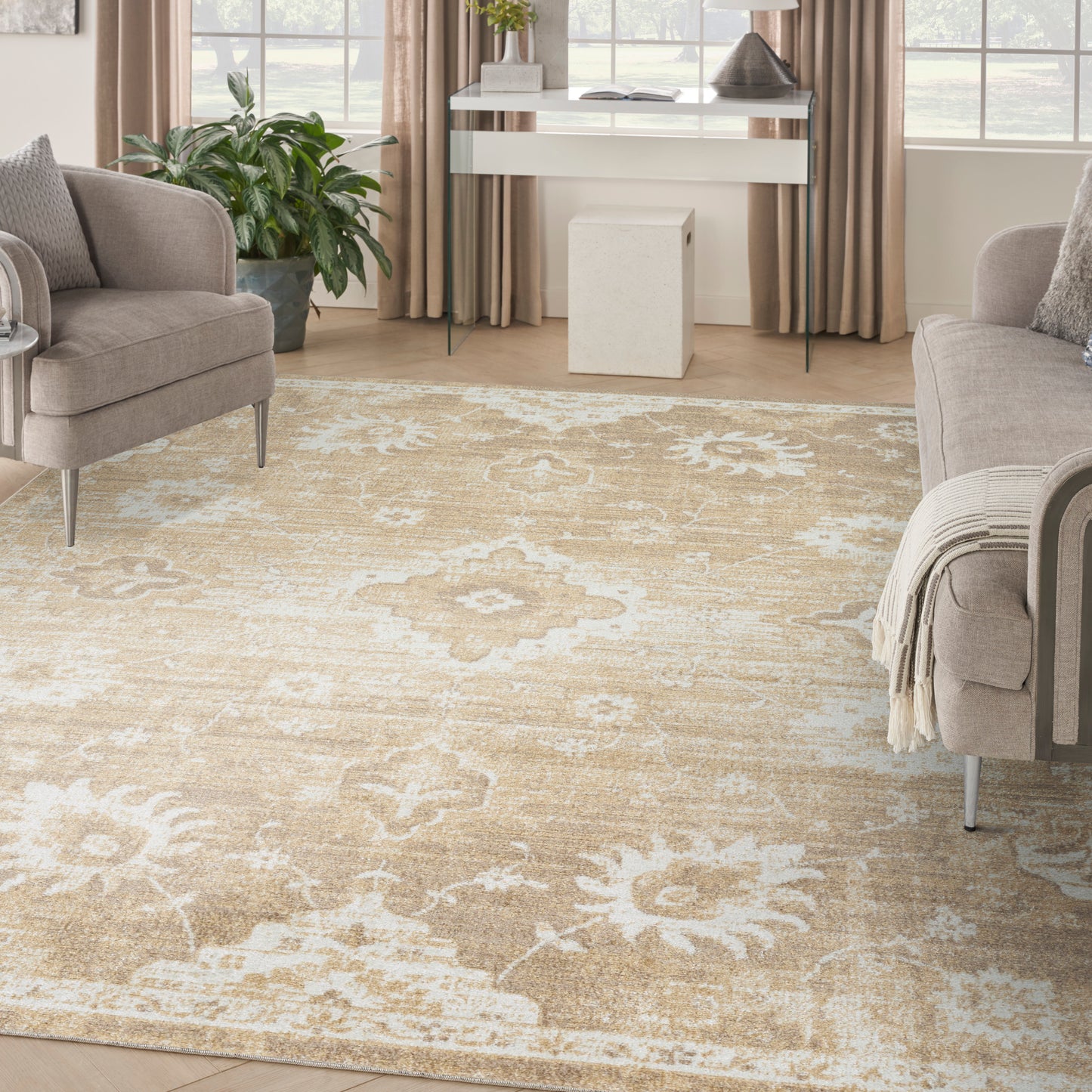 Large beige floral-pattern area rug in a neutral living room with taupe fabric sofas and plants.