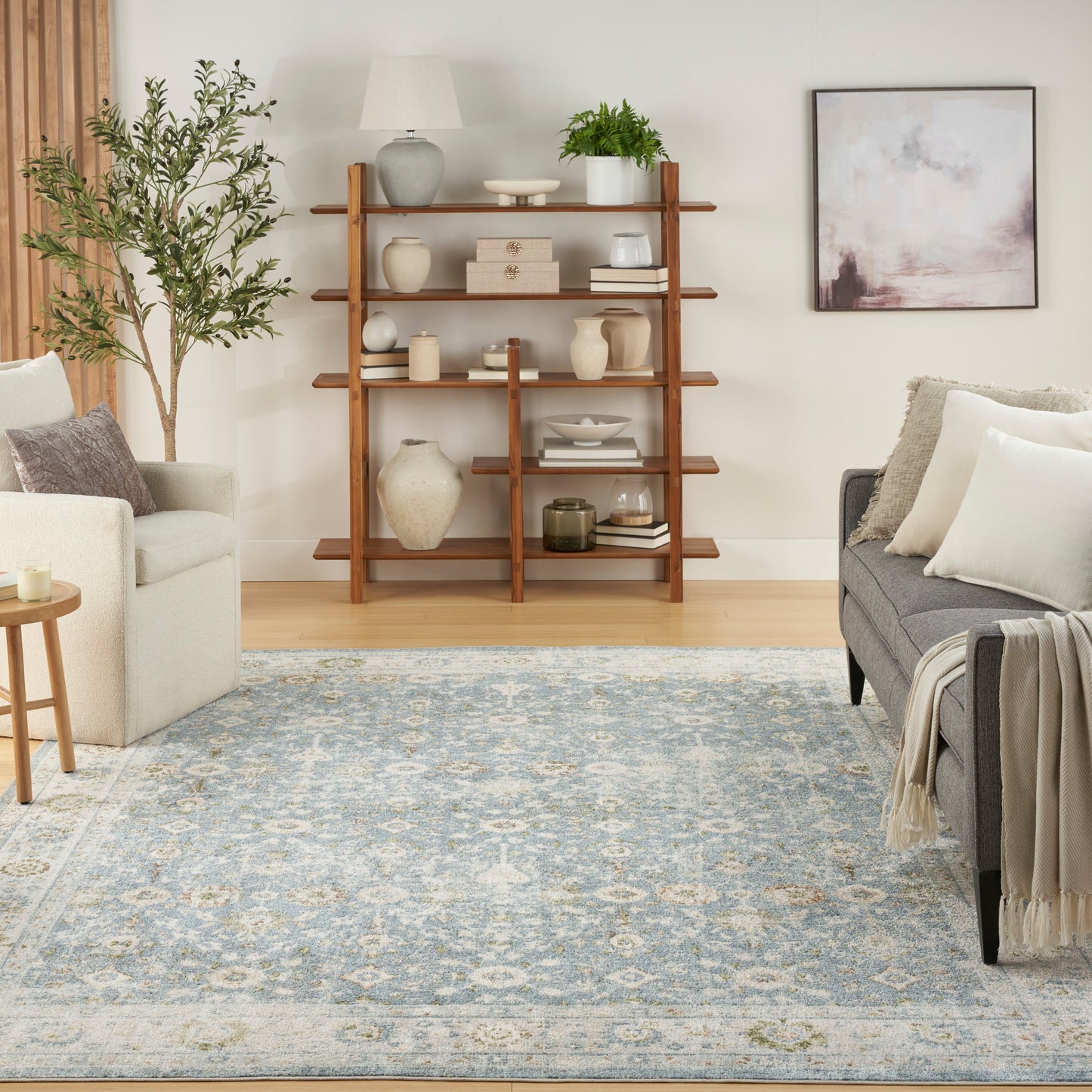 Living room with tall wooden ladder shelf of ceramics and books, potted plant, beige/gray sofas, blue patterned rug.