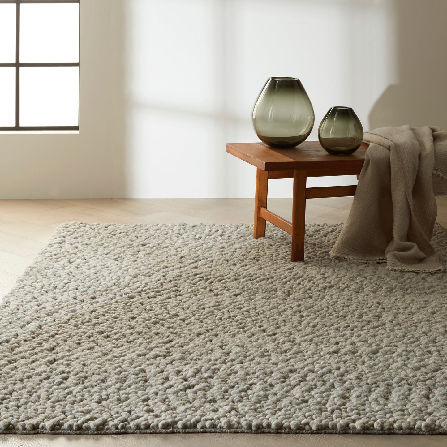 Beige shag rug on a wooden floor with a draped blanket.