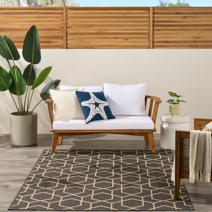 Wooden outdoor sofa with white cushions, navy starfish pillow and cream pillow; large potted plant, geometric rug, wooden slat fence.