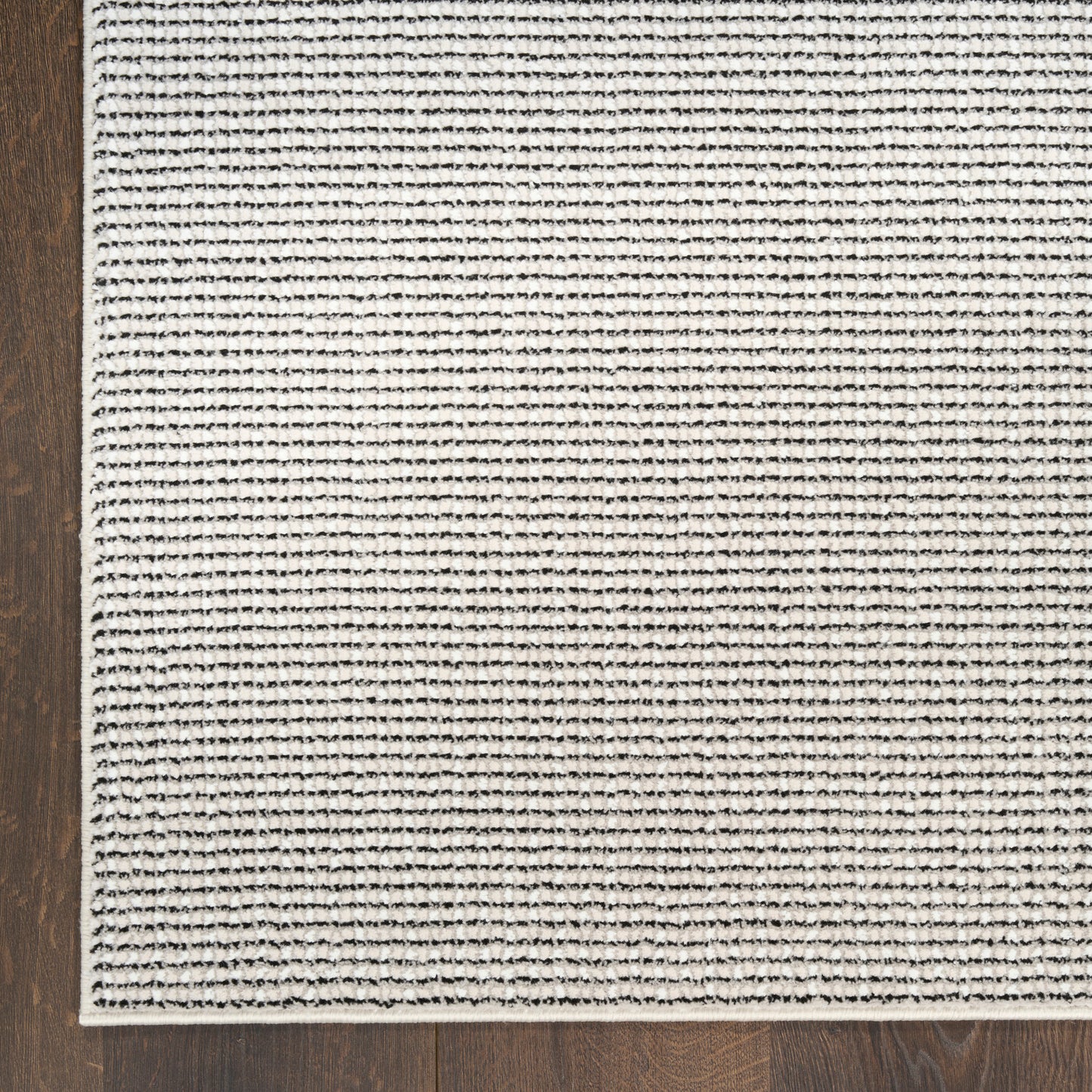 Beige woven area rug with thin black horizontal stripes on a dark wood floor.