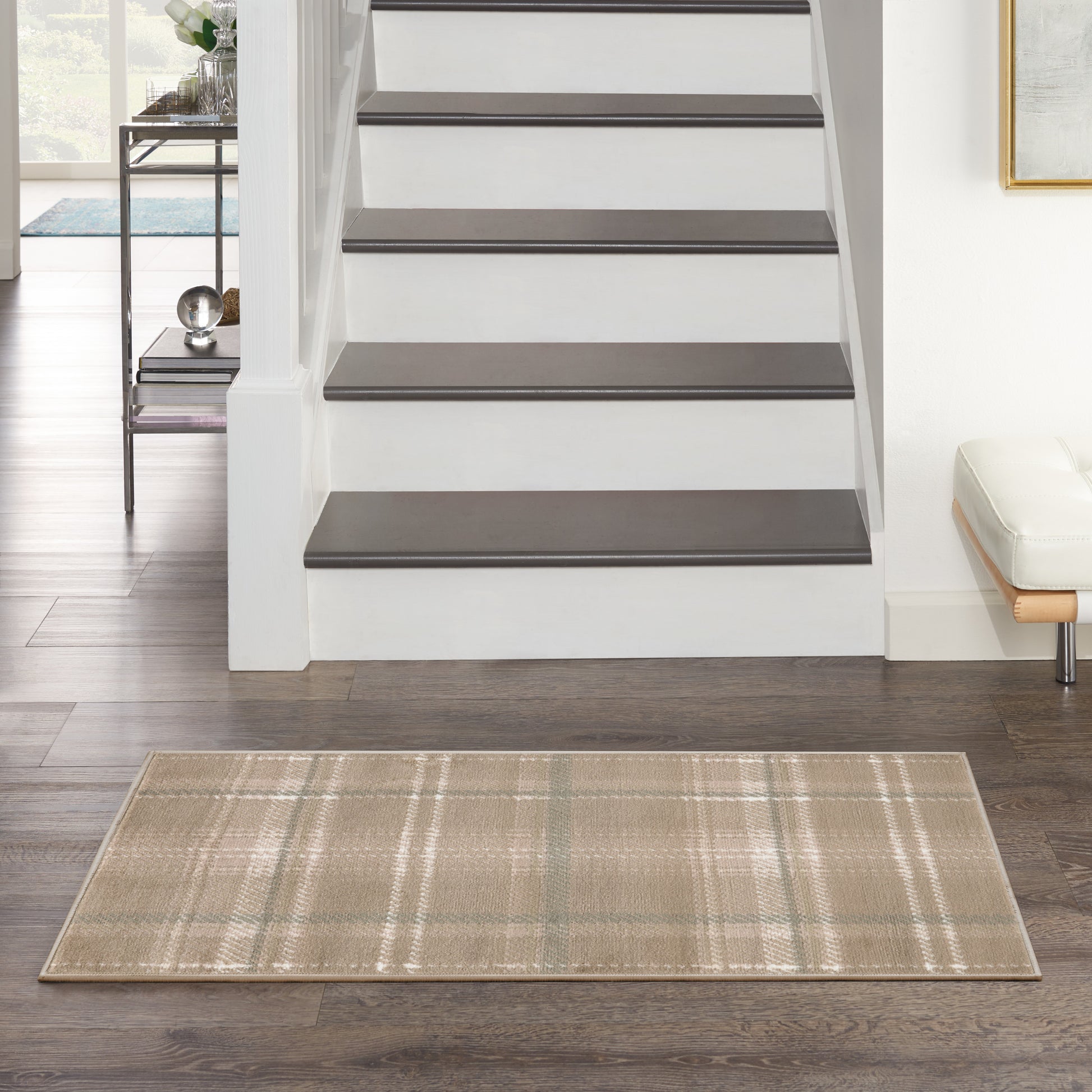 Beige plaid area rug on dark wood floor before a white staircase with dark brown treads; modern entryway.