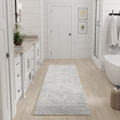 Bright white bathroom with light wood floor, gray runner, white vanity, botanical prints, glass shower, freestanding tub.