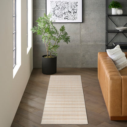 Beige striped runner rug on light wood floor beside a tan leather sofa, with a potted plant, concrete wall and abstract art.