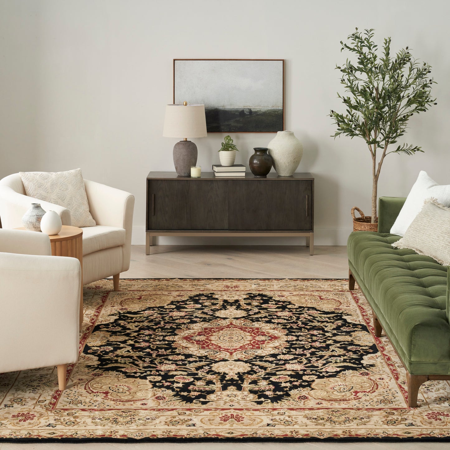 Contemporary living room with dark wood console, beige armchairs, green tufted sofa, ornate oriental rug & plant.