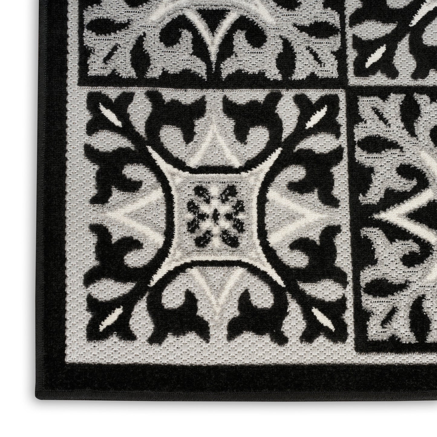 Close-up of black and white patterned rug with ornamental floral tile motifs, bordered edge, textured loop pile.