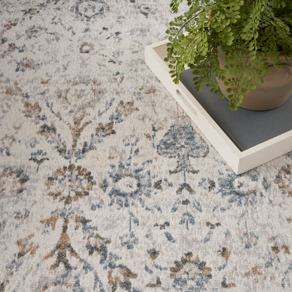 Light vintage floral area rug in blue, gray, beige; potted fern on a white tray atop it.