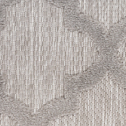 Close-up of light gray woven rug showing geometric block pattern and plush fringe edge.