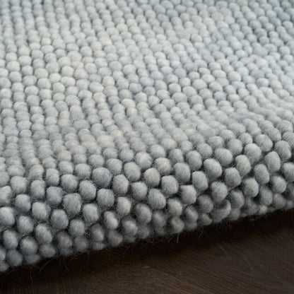 Close-up of a soft gray boucle rug with dense rounded loop fibers on dark wood floor.