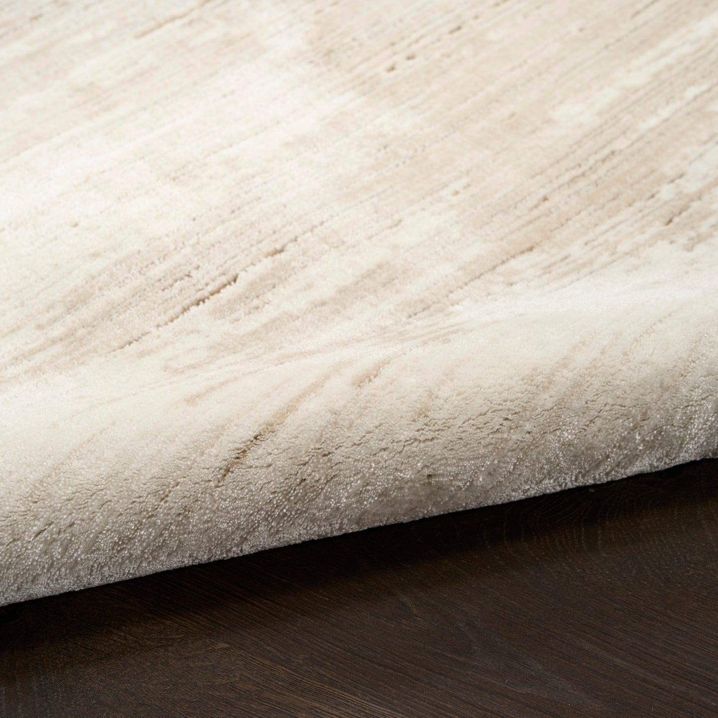 Close-up of a cream beige plush rug, edge curling over a dark wood floor.