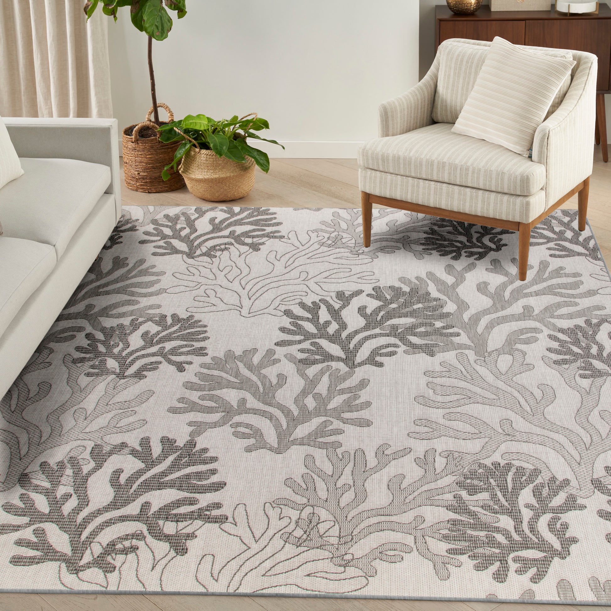 Light gray rug with dark gray coral pattern, beige upholstered armchair on wooden legs, light sofa, and woven plant baskets.