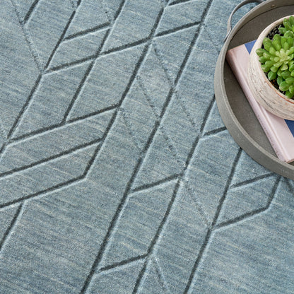 Blue-gray geometric-pattern rug with chevron diamond motif; round metal tray holds a succulent and books.