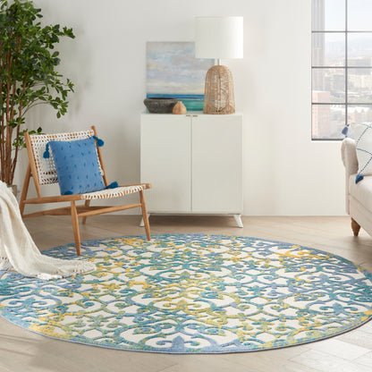 Bright living room with a round blue-yellow rug, woven chair with blue cushion, white cabinet, wicker lamp, plant, and view.