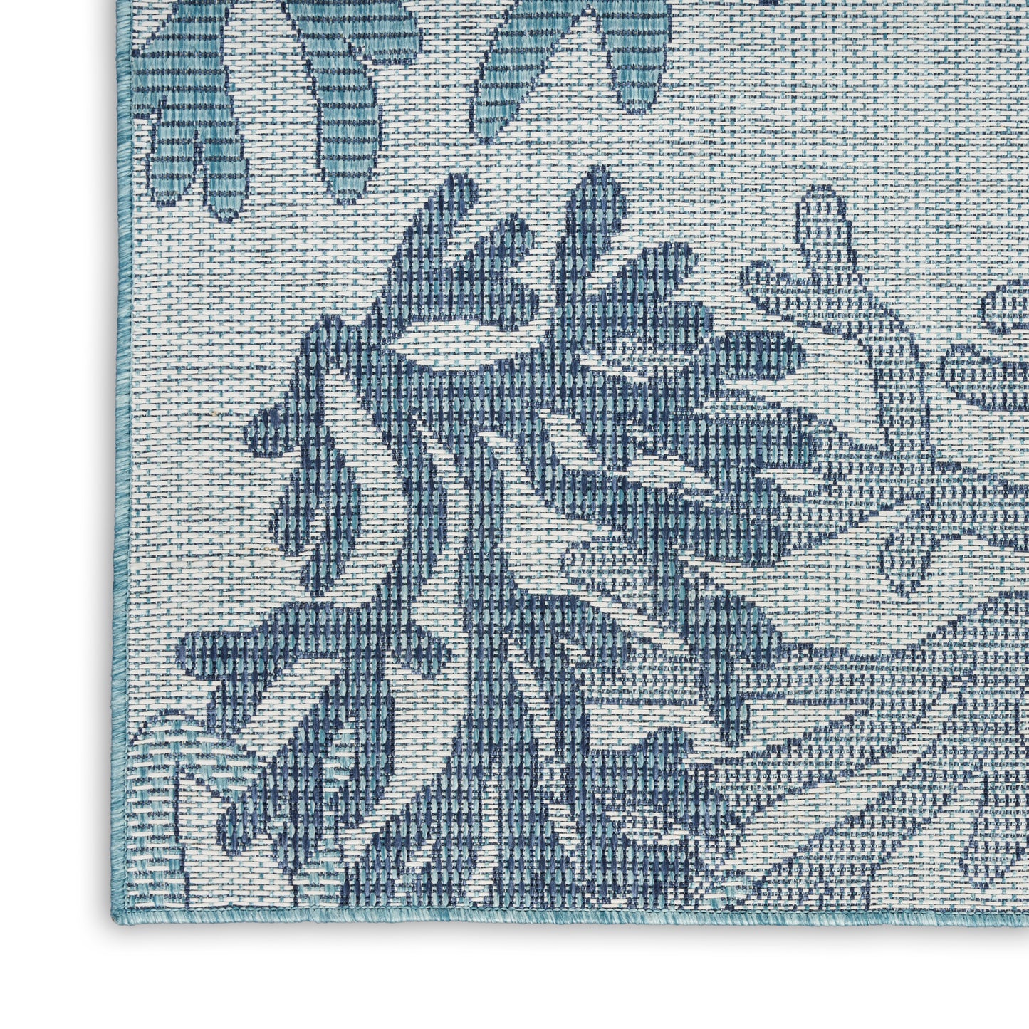 Blue damask-pattern woven rug corner with teal edge trim on beige background.
